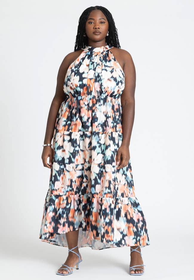 model poses in a halter neck floral midi dress with heeled sandals
