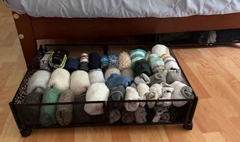 a reviewer photo of the same bed with the rolling bin pulled out and filled with socks 