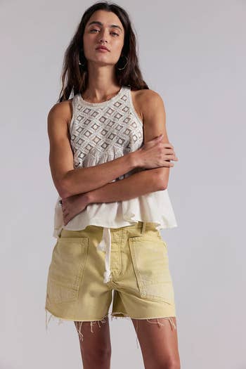 Model in sleeveless boho-style top and frayed shorts, with arms crossed, posing confidently for a casual fashion shoot