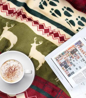 overhead shot of a mug and magazine on top of the reindeer throw blanket to show the blanket's print up close