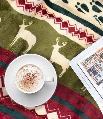 overhead shot of a mug and magazine on top of the reindeer throw blanket to show the blanket's print up close