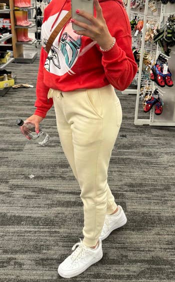 Person successful a graphic sweatshirt and joggers holding a h2o vessel successful a store aisle with displayed products successful the background