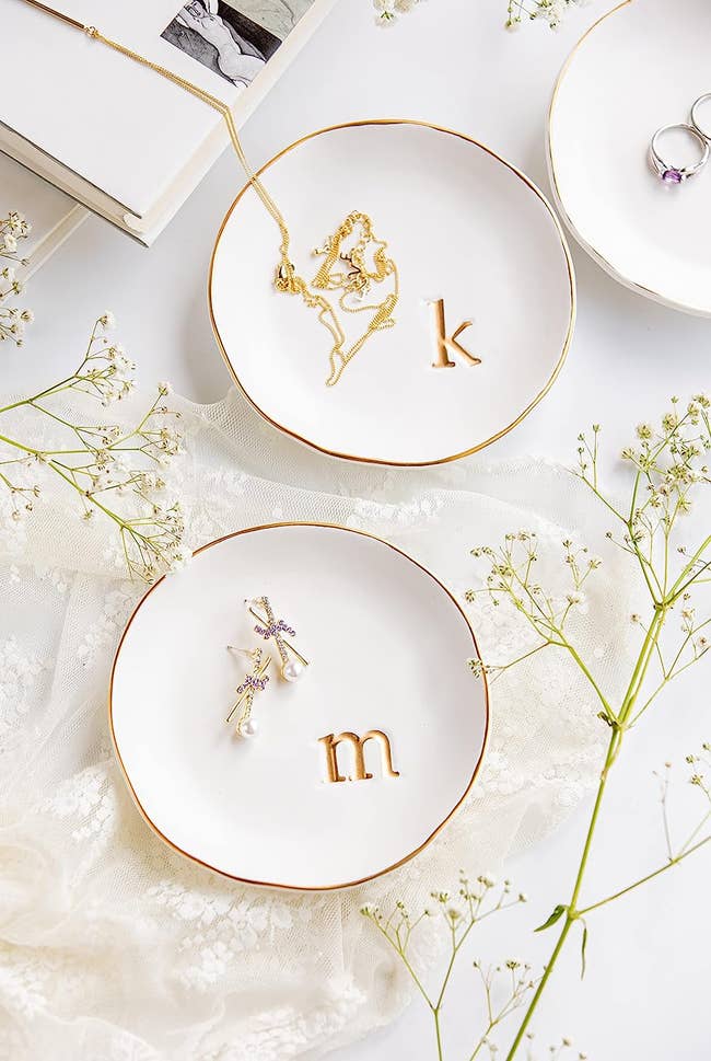 Small white round ceramic dishes with gold detailed edges and a pressed lowercase monogram letter on the bottom right side 
