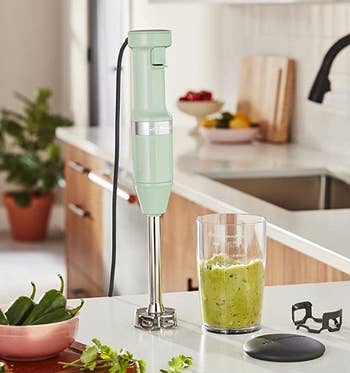 the light green immersion blender on a counter next to a container of guacamole