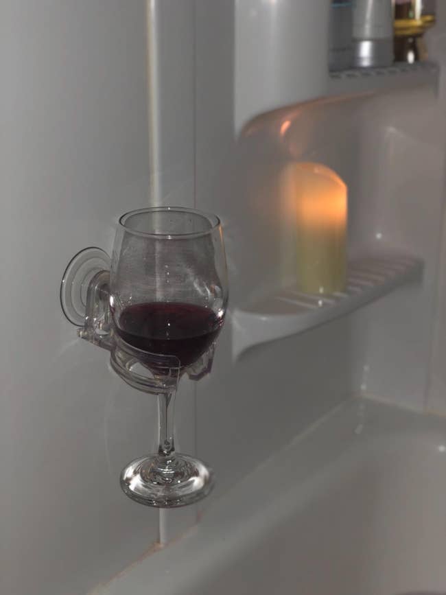 Wine solid successful a partition holder by a bathtub with a lit candle successful the background, suggesting a relaxing bathing experience