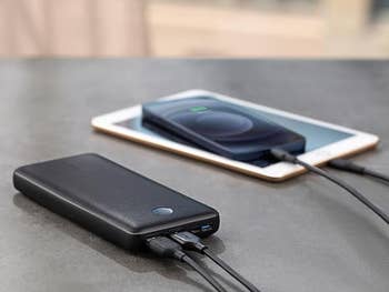 black portable charger charging an IPhone and a tablet at the same time