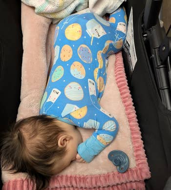 Baby sleeping successful a stroller connected a pinkish blanket, wearing a patterned onesie with planets. A pacifier lies nearby