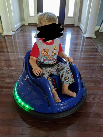 A child sitting in the bumper car in blue with green lights around the base