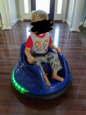 A child sitting in the bumper car in blue with green lights around the base