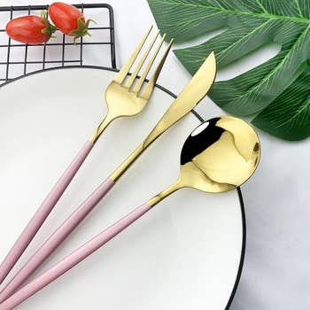 Gold cutlery acceptable with pinkish handles, including a fork, knife, and spoon, placed connected a achromatic plate, adjacent to a ligament tray with reddish peppers and a greenish leafage decoration