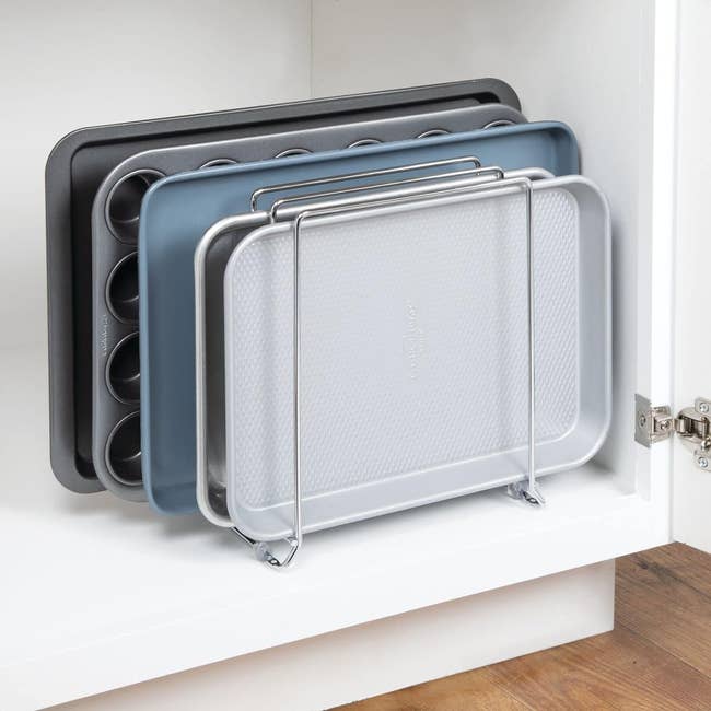 Various-sized baking sheets and a cooling rack stored upright in a kitchen cupboard