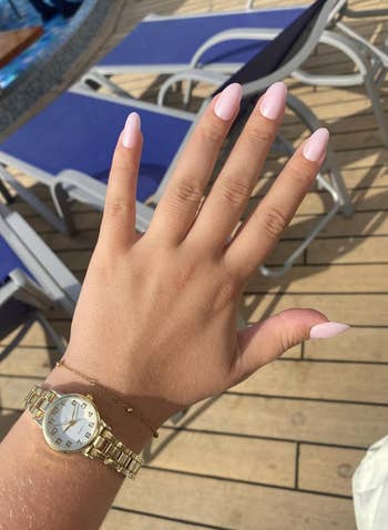 Hand with manicured nails and a golden  ticker  and bracelet, positioned implicit    lounge chairs connected  a woody  deck, suggesting a relaxed setting