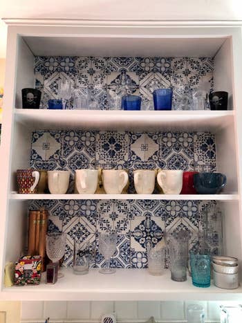A reviewer's kitchen shelf with assorted mugs, glasses, and a pitcher displayed against a patterned backdrop