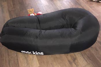 Reviewer image of black inflatable couch on hardwood floor with teddy bear on top of it