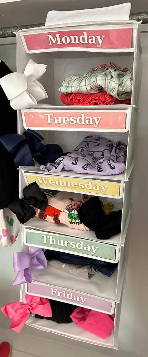 A hanging organizer with labeled compartments for each weekday (Monday to Friday), each containing neatly folded apparel and accessories