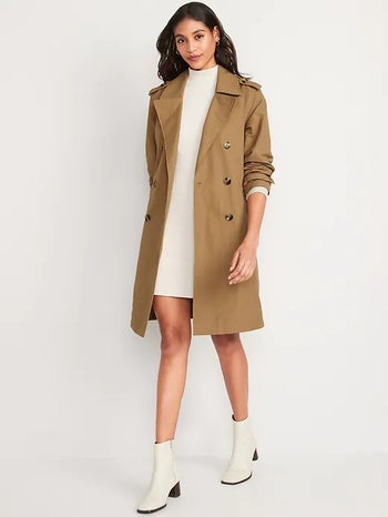 model wearing the tan trench over a white dress with white boots