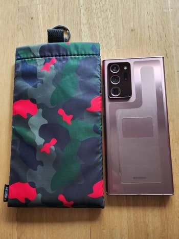 Camouflage phone pouch next to a modern smartphone on a wooden surface