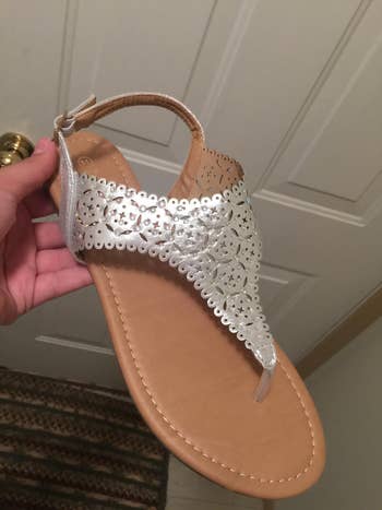 Reviewer holding brown and silver thong gladiator sandals with tiny rhinestones decorating the top