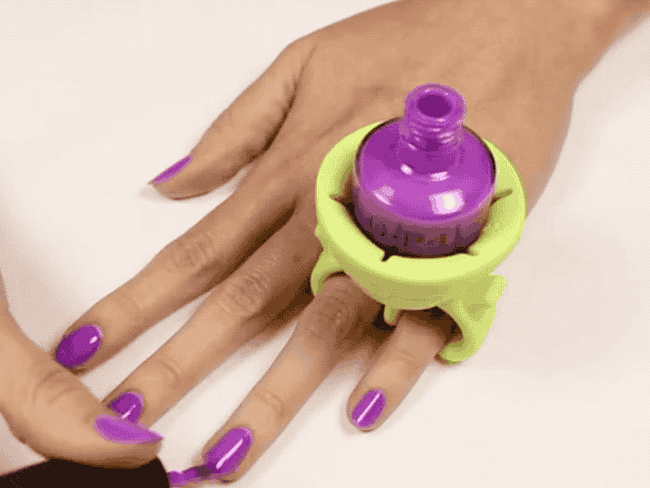 A person's hand with purple nail polish using a wearable nail polish bottle holder while painting nails
