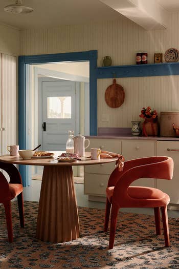 Interior kitchen scene with a round table set for a meal and two velvet chairs. Contemporary cozy design