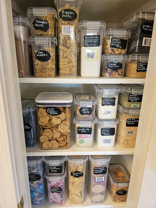 Organized pantry shelves with labeled wide containers holding assorted pantry staples similar pasta, cereals, and baking ingredients
