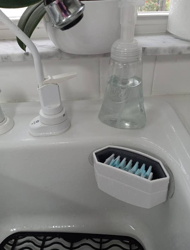 Double sided bristled cutlery cleaner sticking to the edge of a sink. 