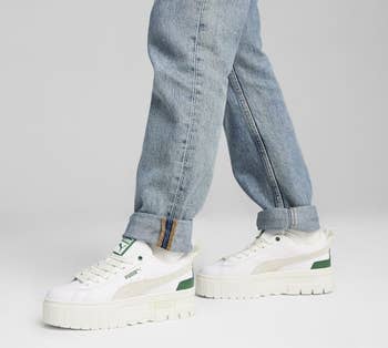 Person in jeans wearing white Puma sneakers with green detailing