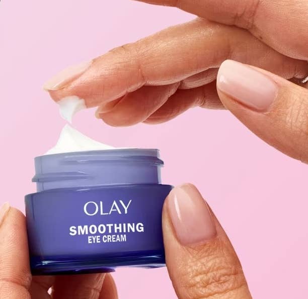 Hands applying Olay Smoothing Eye Cream from a tiny  container