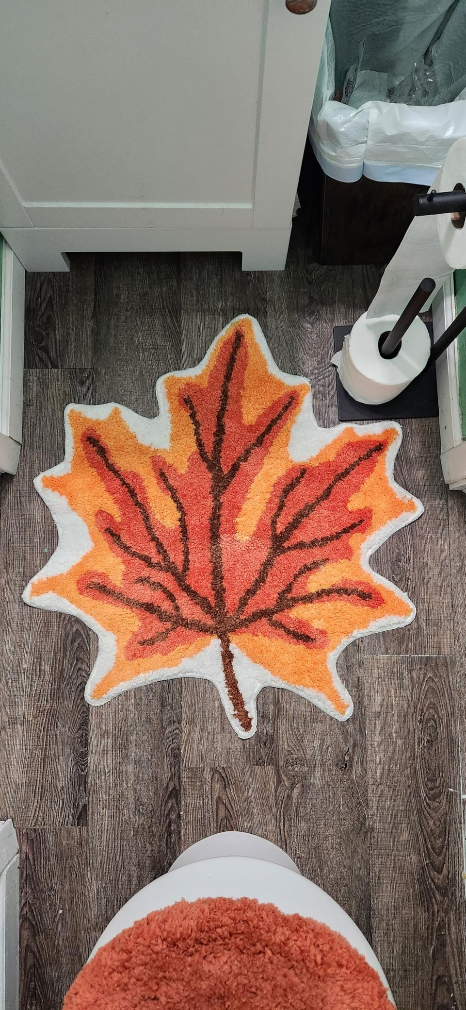 Leaf-shaped bath  rug with autumn plan  connected  woody  floor, adjacent  to a toilet and toilet paper
