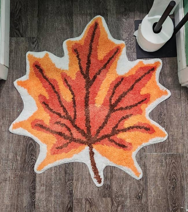 Leaf-shaped bath rug with autumn plan connected woody floor, adjacent to a toilet and toilet paper