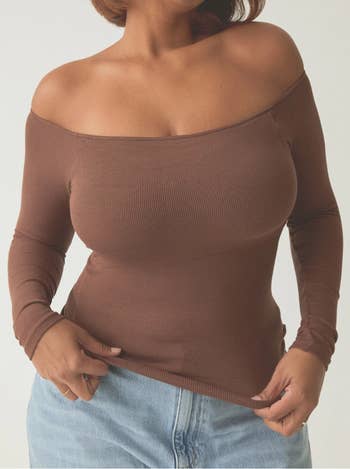 Person wearing an off-shoulder, long-sleeved apical  paired with denim jeans