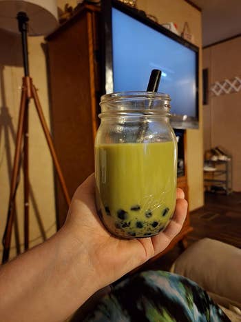 Person holding a mason jar with boba milk tea