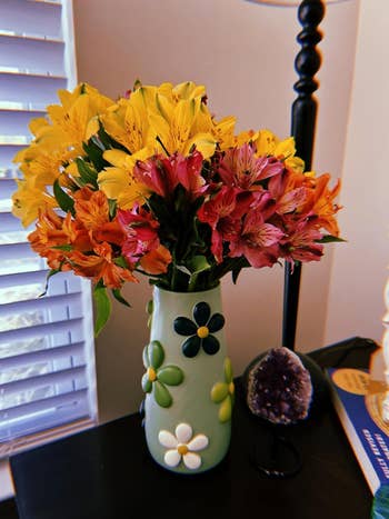 A vibrant bouquet of yellow and red flowers arranged in a decorative vase with floral motifs