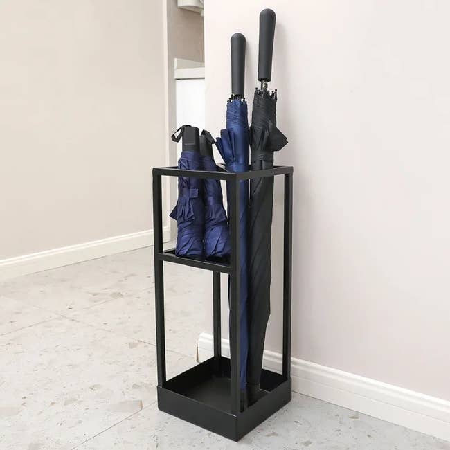 a black stand with a built-in shelf for holding mini umbrellas upright as well as a section for full-size umbrellas