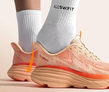 Person wearing orangish  and beige diversion  shoes with heavy   soles, paired with achromatic  socks labeled 