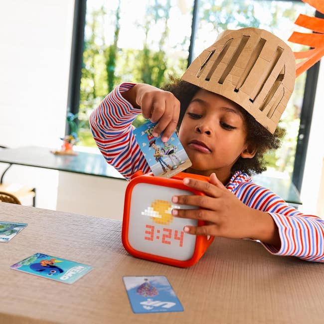 Child successful cardboard helmet plays with interactive timepiece and cards astatine home