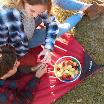lifestyle photo of a couple eating fruit on couglan's picnic blanket