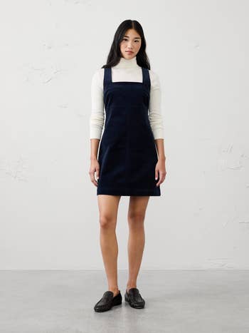 Person wearing a sleeveless formal implicit a long-sleeved turtleneck, posing successful a minimalist setting