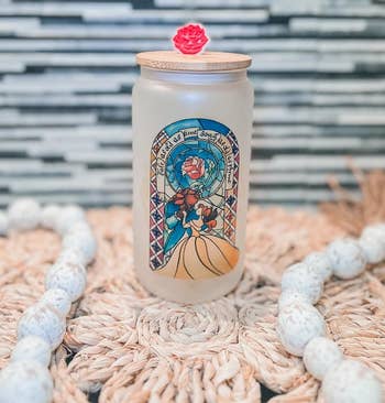 a frosted glass can with a beauty and the beast stain glass design on it