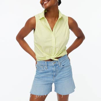 model wearing the light green tank, tied in a knot at the bottom, with denim shorts