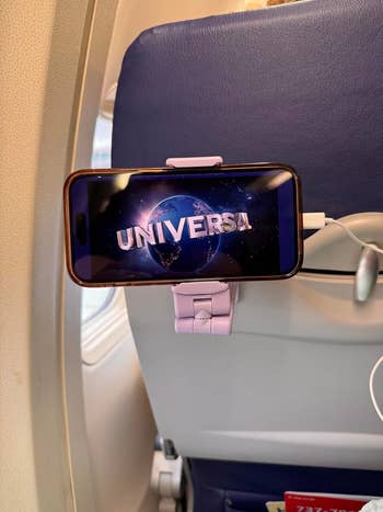 A smartphone mounted on an airplane seatback shows the Universal Pictures logo 