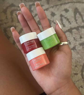 reviewer holding three small containers of lip mask in berry, pomegranate, and lime 