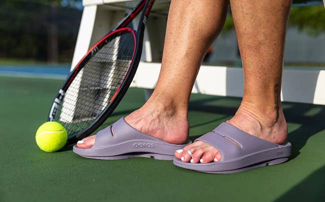 tennis player wearing lavender colored oofos slides