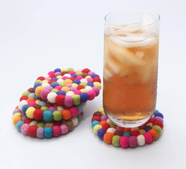a cold drink resting on one of the rainbow coasters next to a stack of three other coasters