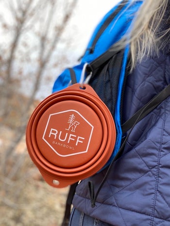 reviewer wearing a backpack with the rust colored, folded down dog bowl attached to it with a carabiner