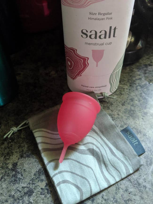 reviewers' pink Saalt menstrual cup next to container and cleaning cloth