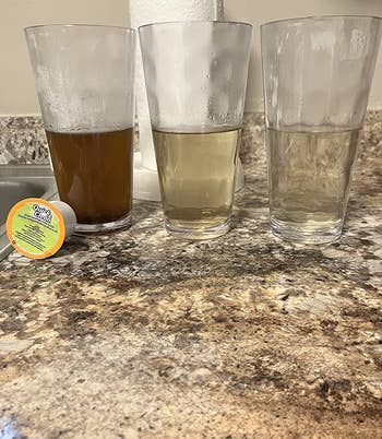 reviewer photo of three glasses containing different colored liquids, from brown to clear, to show how effectively the cleaning k-cups cleaned their coffee maker