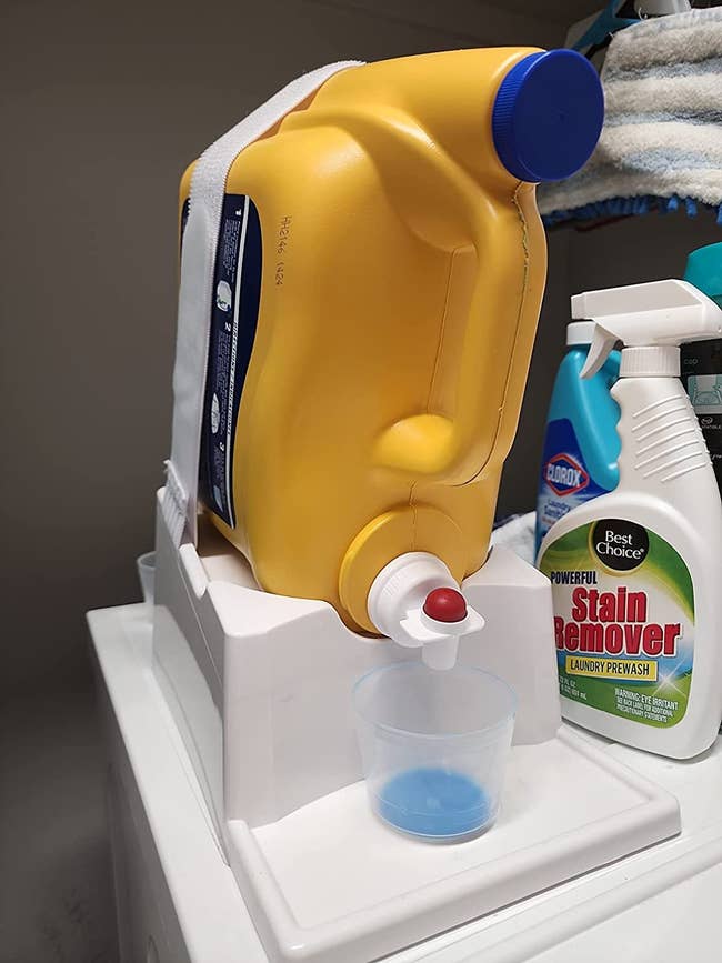 reviewer image of a jug of detergent strapped to the laundry station organizer with a cup under its spout