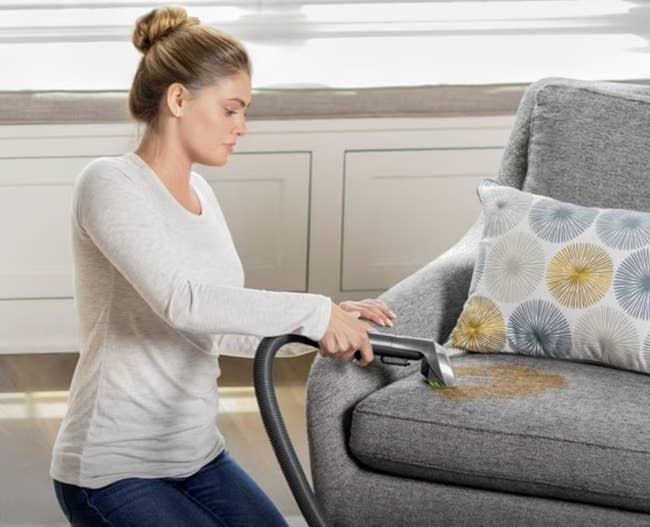 Person utilizing a handheld vacuum to cleanable a spill connected a sofa successful a surviving room
