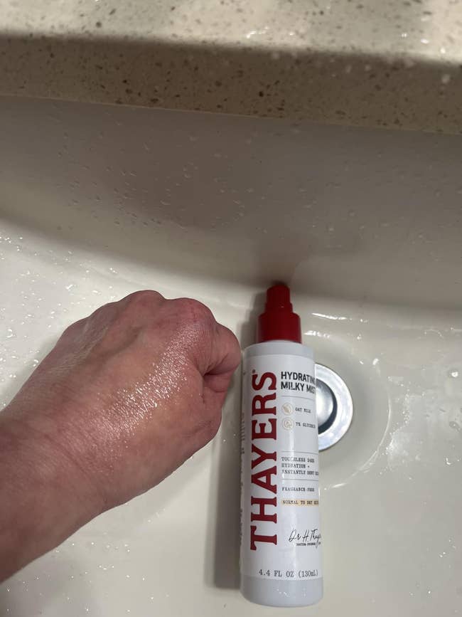 A reviewer's Hand applying Thayers Hydrating Milky Mist successful  a bath  sink